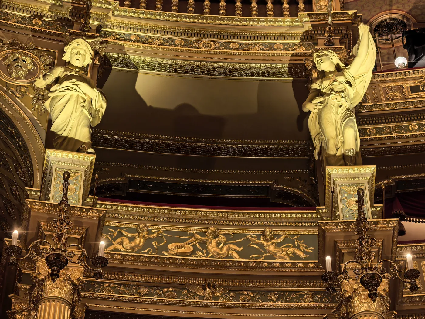 Two gilded figures flanking a box with a gold balustrade in the auditorium
