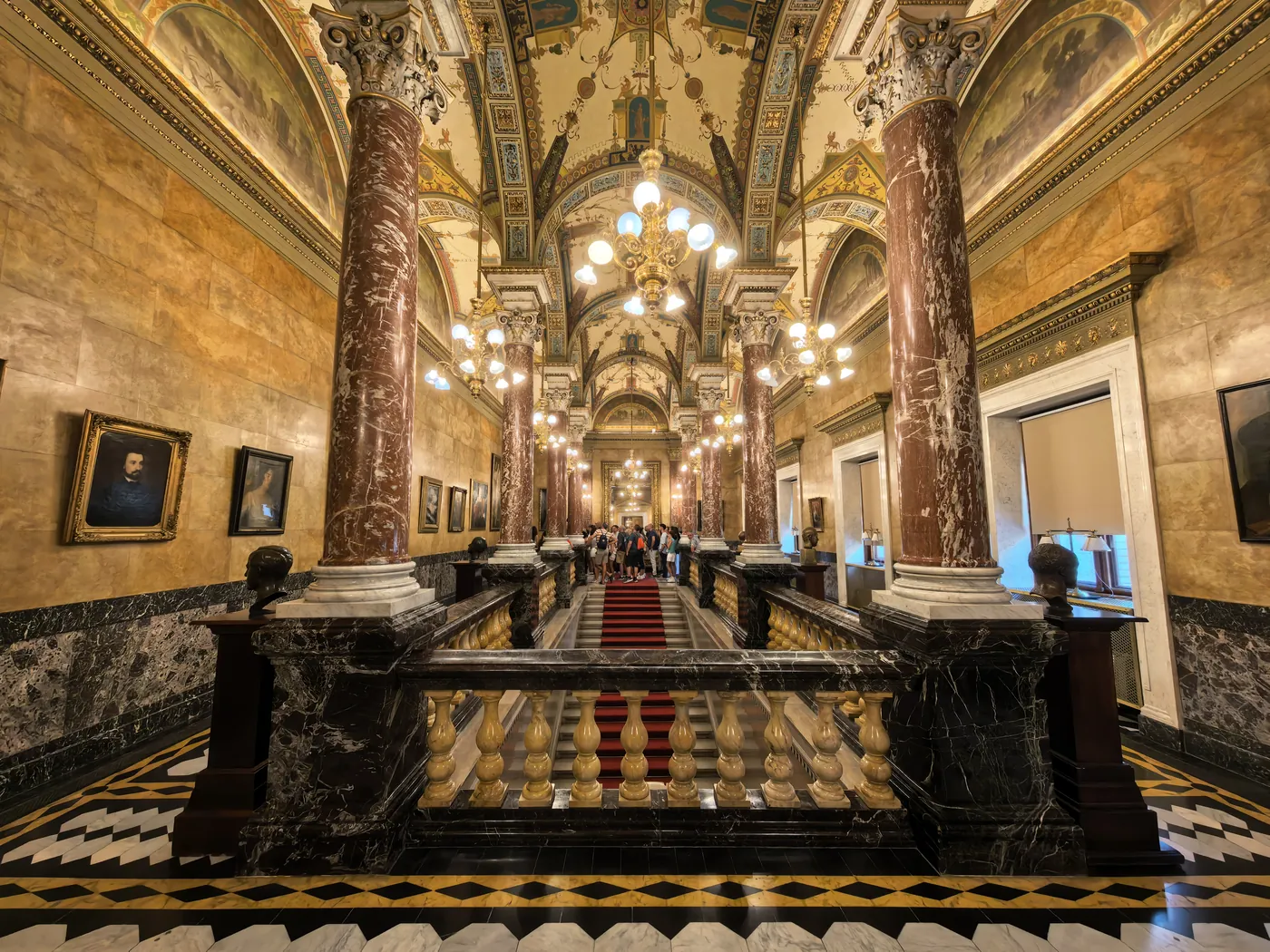 A long hall of marble columns, framed portraits and chandeliers inside the Opera House