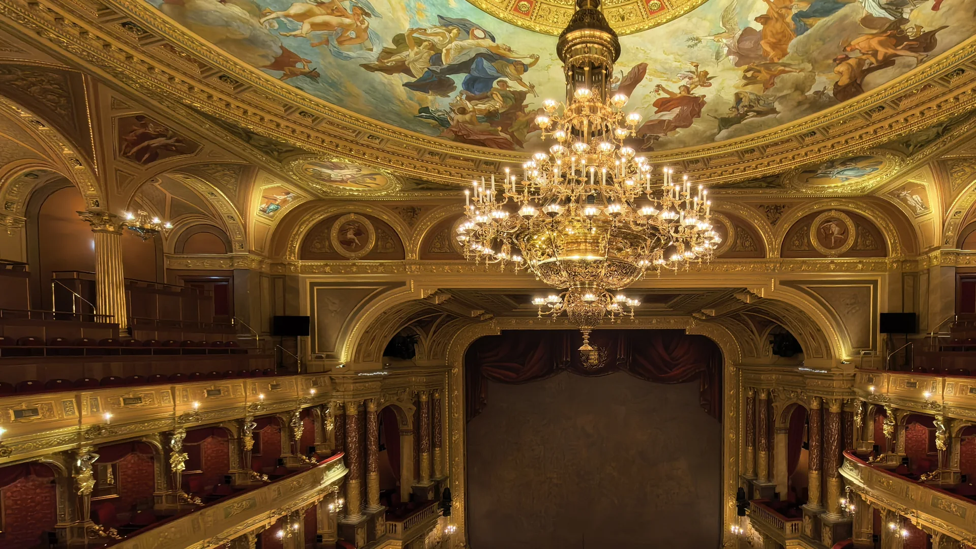 The auditorium of the Hungarian State Opera House, with a gilded chandelier hanging below the painted ceiling in front of the stage